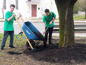 two student pour dirt from a wheelbarrow