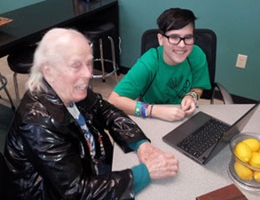 teen works on a computer with a senior citizen